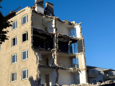 Açık mavi gökyüzü altında kısmen yıkılmış bir apartman..