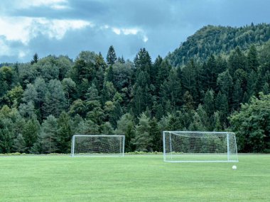 Bereketli ormanda, bulutlu gökyüzünün altında dağlık zemin olan boş bir futbol sahası..