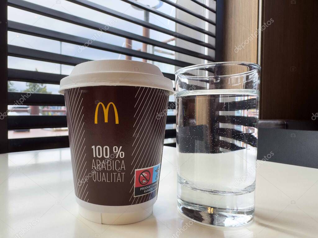 Coffee and water on table at fast food restaurant with window blinds.