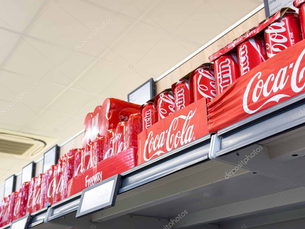 Coca-cola cans on supermarket shelf displaying iconic red branding.