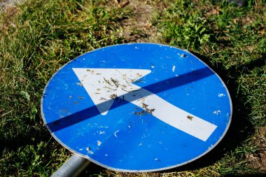 Düşmüş mavi trafik işareti ve çimlerin üzerinde beyaz ok.