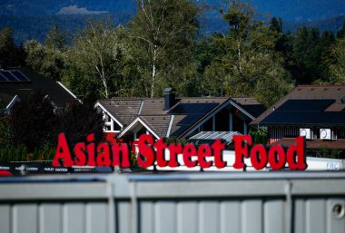 Faaker See, Avusturya - 01 Eylül 2025: Asya Sokak Gıda tabelası, yerel mutfağı ön plana çıkaran resimli ev ve ağaçların önünde duruyor