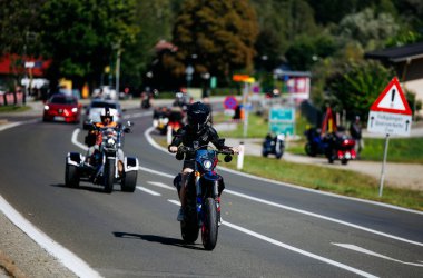 Faaker See, Avusturya - 01 Eylül 2025: Virajlı yolda siyah dişli motosikletli bir motosikletli, diğer sürücüler de eşlik ederek Avrupa Bisiklet Haftası 'nın heyecanını yakalıyor