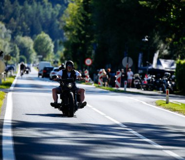 Faaker See, Avusturya - 01 Eylül 2025: Harley-Davidson motosikletli motosiklet Avrupa Bisiklet Haftası boyunca arka planda ağaçlar ve diğer motosikletçilerle birlikte manzaralı yolda ilerliyor