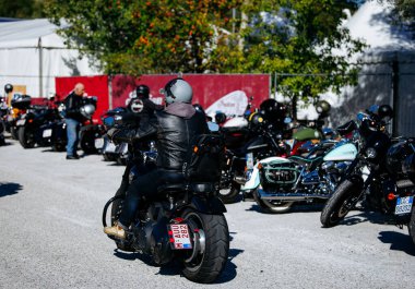 Faaker See, Avusturya - 01 Eylül 2025: Deri ceketli bisikletçi Avrupa Bisiklet Haftası 'nda motosiklet sürüyor, etrafı Harley-Davidson motosikletleri ve canlı açık hava setiyle çevrili.