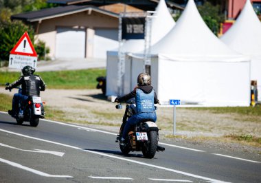 Faaker See, Avusturya - 01 Eylül 2025: Motosikletli bisikletliler Avrupa Bisiklet Haftası boyunca yol boyunca seyahat ederken, festival çadırları ve yeşillikler sahneyi çevreledi