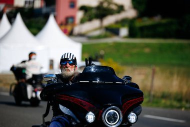 Faaker See, Avusturya - 01 Eylül 2025: Çizgili kasklı yaşlı adam Avrupa Bisiklet Haftası 'nda siyah Harley-Davidson motosikleti sürüyor, etkinliğin ruhunu yakalıyor