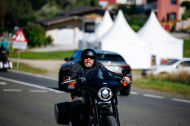 Faaker See, Avusturya - 01 Eylül 2025: Avrupa Bisiklet Haftası boyunca siyah Harley-Davidson motosikletli motosikletli erkek motosiklet sürücüsü, motosiklet kültürünün ruhunu yakaladı