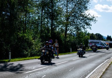 Faaker See, Avusturya - 01 Eylül 2025: Motosikletçiler Avrupa Bisiklet Haftası boyunca Harley-Davidson bisikletleri ve yemyeşil otlakların yer aldığı manzaralı bir yolda gezintiye çıktılar
