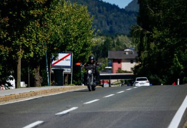 Faaker See, Avusturya - 01 Eylül 2025: Motosiklet meraklısı Avusturya 'da canlı ağaçlar ve dağlarla muhteşem bir zemin oluşturan pitoresk bir yolda ilerliyor