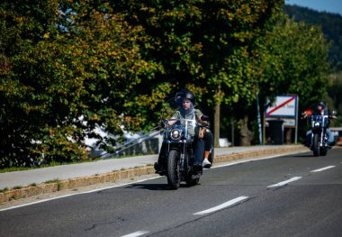 Faaker See, Avusturya - 01 Eylül 2025: Harley-Davidson motosiklet meraklısı Avrupa Bisiklet Haftası boyunca verimli ağaçlar ve parlak gökyüzü ile pitoresk yol boyunca geziyor