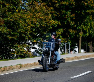 Faaker See, Avusturya - 01 Eylül 2025: Erkek motorcu, canlı ağaçlarla çevrili Avrupa Bisiklet Haftası boyunca Harley-Davidson motosikleti sürmekten keyif alıyor