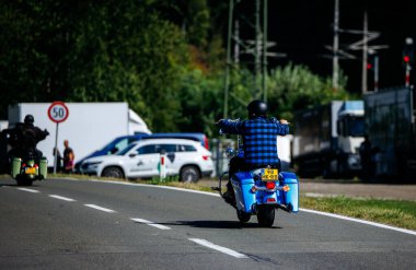 Faaker See, Avusturya - 01 Eylül 2025: Mavi ekose gömlek giyen bisikletçi Avrupa Bisiklet Haftası boyunca motosiklet sürüyor, macera ruhunu yakalıyor