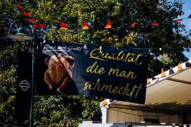 Faaker See, Avusturya - 01 Eylül 2025: Harley-Davidson pankartı Avrupa Bisiklet Haftası 'nda renkli dekorasyonlar ve canlı ambiyansla çevrili ızgara tavuk içeriyor