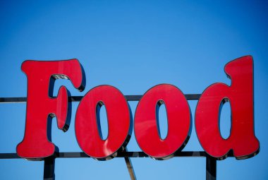 Faaker See, Avusturya - 01 Eylül 2025: Parlak kırmızı gıda işareti mavi gökyüzüne karşı duruyor, açık hava yemekleri ve aşçılık keyfi için davetkar bir ortam yaratıyor