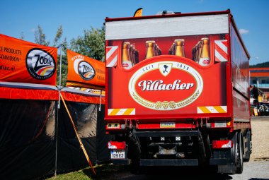 Faaker See, Avusturya - 01 Eylül 2025: Kilacher bira logolu kırmızı kamyon Avrupa Bisiklet Haftası 'na park edilmiş, Harley-Davidson çadırları canlı bir festival sahnesi yaratıyor