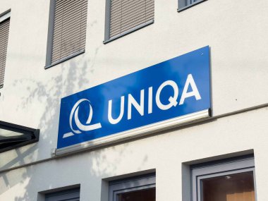 Moosburg, Avusturya - 27 Ağustos 2025: UNIQA logosu, günışığıyla aydınlanan ve canlı bir atmosfer yaratan çağdaş bir bina cephesinde sergilenmektedir