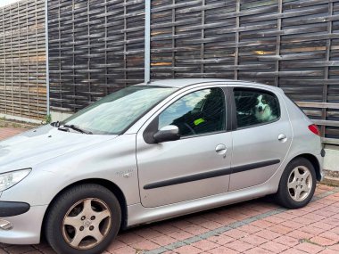 Moosburg, Avusturya - 27 Ağustos 2025: Pencereden dışarı bakan bir köpekle sokağa park edilmiş gümüş bir hatchback, büyüleyici bir şehir manzarası yaratıyor