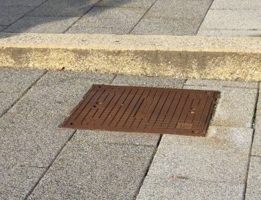 Kare rögar kapağı desenli beton kaldırımda.