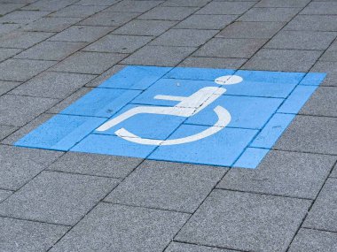 Gri kare asfaltın üzerine mavi tekerlekli sandalye erişilebilir tabelası.