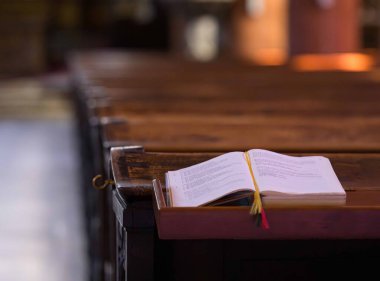 Villach, Avusturya - Eylül 04, 2025: Açık kitap huzurlu kilisenin iç kısımlarındaki ahşap sıralarda uzanıyor, sakin atmosferi ve sıcak aydınlatmayı vurguluyor