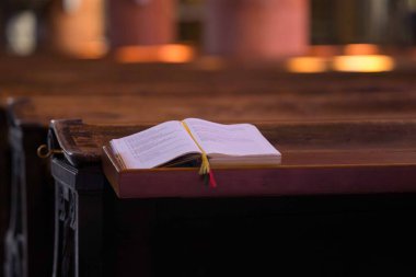 Villach, Avusturya - Eylül 04, 2025: Huzurlu kilise ortamındaki ahşap sıralara yerleştirilmiş açık kitap, dingin ve ruhani ortamı vurguluyor