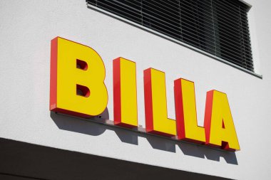 Villach, Avusturya - Eylül 04, 2025: BILLA işareti kırmızı çizgili koyu sarı harfler içeriyor, beyaz bir duvara yaslanmış, marka kimliğini vurguluyor