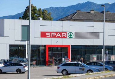 Villach, Avusturya - Eylül 04, 2025: SPAR süpermarketi, park halindeki araçlar ve manzaralı dağlarla çevrili, berrak markalaşmış modern bir tasarıma sahiptir.