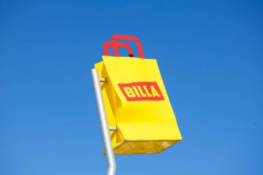 Villach, Avusturya - Eylül 04, 2025: BILLA marka işareti açık mavi gökyüzüne karşı belirgin bir şekilde sarı ile gösterildi, marka görünürlüğü ve renk karşıtlığını vurguluyor