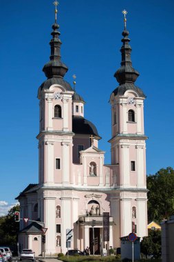 Villach, Avusturya - Eylül 04, 2025: Çarpıcı pembe kilise canlı mavi gökyüzü ve kentsel manzara ile çevrili ikiz kuleler ve süslü detaylar içeriyor