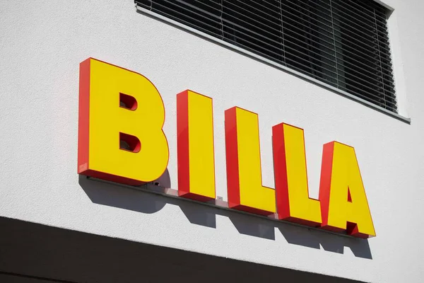 Villach, Avusturya - Eylül 04, 2025: BILLA işareti kırmızı çizgili koyu sarı harfler içeriyor, beyaz bir duvara yaslanmış, marka kimliğini vurguluyor