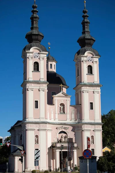 Villach, Avusturya - Eylül 04, 2025: Sersemletici pembe kilise canlı manzara ve açık mavi gökyüzü ile çevrili ikiz kuleler ve süslü detaylar içerir.