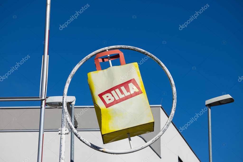 Villach, Austria - September 04, 2025: BILLA sign displays a yellow shopping bag against a bright blue sky, emphasizing brand visibility and urban atmosphere