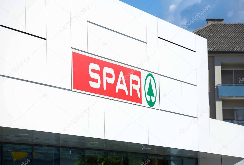 Villach, Austria - September 04, 2025: SPAR supermarket facade features bold red logo and green symbol under clear blue sky, highlighting contemporary design