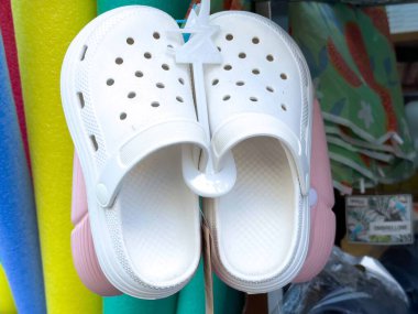 Graz, Avusturya - Eylül 06, 2025: Canlı havuz şamandıraları ve plaj eşyalarıyla dolu bir mağazada beyaz takunyalar sergileniyor.