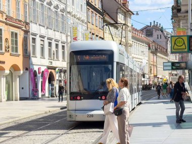 Graz, Avusturya - Eylül 06, 2025: Yoğun caddede yayalar ve canlı kentsel atmosfer yaratan dükkanlarla modern tramvay istasyonuna yaklaşıyor