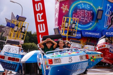 Villach, Avusturya - 30 Temmuz 2025: İki genç çocuk renkli dekorasyonlar ve hareketli ambiyanslarla çevrili Villacher Kirchtag festivalinde eğleniyor