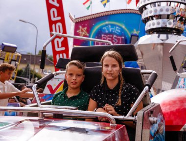 Villach, Avusturya - 30 Temmuz 2025: İki çocuk heyecan verici bir şekilde Villacher Kirchtag 'de oturuyorlar, arka planda hareketli gösteriler ve şenlikli dekorasyonlar var.