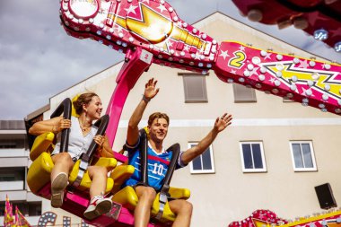 Villach, Avusturya - 30 Temmuz 2025: Genç bir çift arka planda canlı renkler ve heyecanla Villacher Kirchtag festivalinde eğleniyor