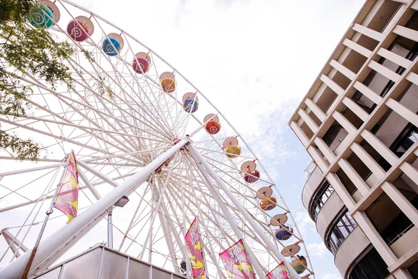 Villach, Avusturya - 30 Temmuz 2025: Dönme dolap Villacher Kirchtag 'deki çağdaş binanın yanında duruyor, kopya uzayı ile canlı ve renkli bir sahne yaratıyor.