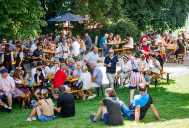 Ossiacher Tauern, Avusturya - 10 Ağustos 2025: Rindfleischfest, güneşli bir park ortamında yemek ve içeceklerin keyfini çıkaran açık hava masalarında toplanmış canlı bir kalabalığa yer veriyor.