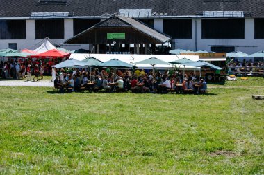 Ossiacher Tauern, Avusturya - 10 Ağustos 2025: Rindfleischfest, güneşli bir açık havada renkli şemsiyeler altında yemek yiyen insanların canlı bir araya gelişini konu alıyor.