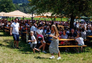 Ossiacher Tauern, Avusturya - 10 Ağustos 2025: Aileler Rindfleischfest 'te bir araya gelerek piknik masalarıyla canlı bir açık hava ortamında yemek ve içeceklerin keyfini çıkarıyorlar