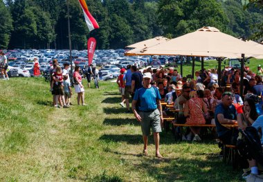 Ossiacher Tauern, Avusturya - 10 Ağustos 2025: Rindfleischfest güneşli bir açık hava ortamında şemsiye altında yiyecek ve içeceklerin keyfini çıkaran canlı bir kalabalığa ev sahipliği yapıyor.