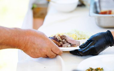 Açık hava etkinliğinde taze pişmiş et ve sebze servis eden eller..