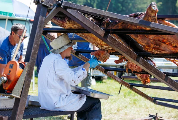 Ossiacher Tauern, Avusturya - 10 Ağustos 2025: Beyaz önlüklü erkek şef Rindfleischfest 'te festival katılımcıları ve açık hava etkinlikleriyle çevrili kızarmış et oyuyor