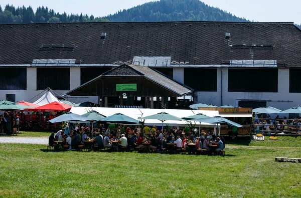Ossiacher Tauern, Avusturya - 10 Ağustos 2025: Rindfleischfest renkli çadırlarla canlı açık hava toplantıları, manzaralı dağ arka planında yemek ve içeceklerden keyif alan insanlar