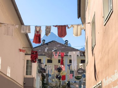 Lienz, Avusturya - 18 Eylül 2025: Dar bir sokaktaki binalar arasında asılı renkli giysiler, arka planda dağların görünmesi