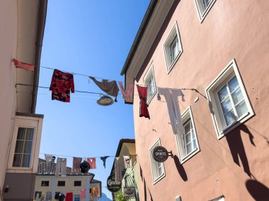 Lienz, Avusturya - 18 Eylül 2025: Parlak mavi gökyüzünün altındaki binalar arasında asılı renkli giysiler, tuhaf bir ara sokakta canlı bir atmosfer yaratıyor