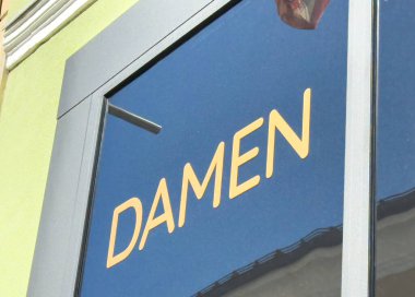 Lienz, Avusturya - 18 Eylül 2025: Damen işareti mağaza vitrininde belirgin bir şekilde gösterilir, güneş ışığını yansıtır ve fotokopi alanı ile canlı bir kentsel atmosfer yaratır